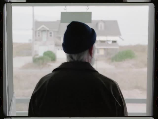 An elderly man walks outside a house