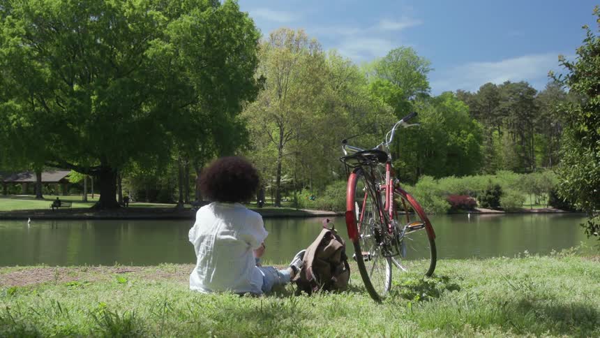 A woman sits in the grass by the pond