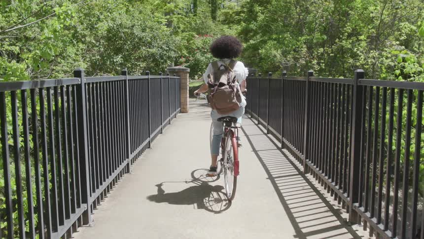 Woman pedals a bike over a bridge near trees