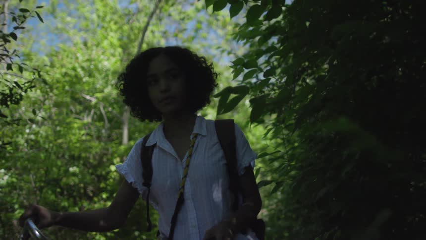 Woman walking a bicycle through tall bushes