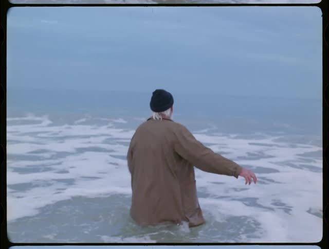 A clothed man walks into an ocean