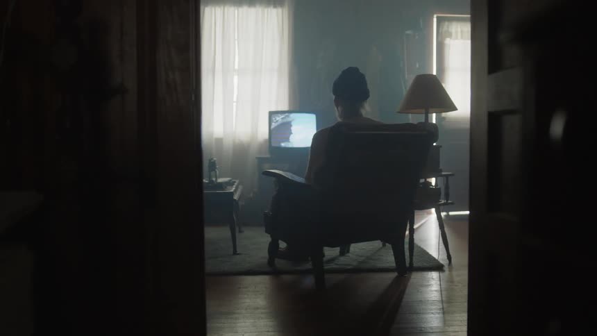 A man wearing a hat sits in a chair watching tv