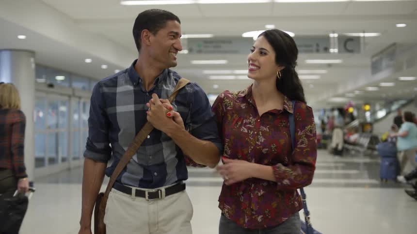 Man and woman smile and hold hands walking through an airport