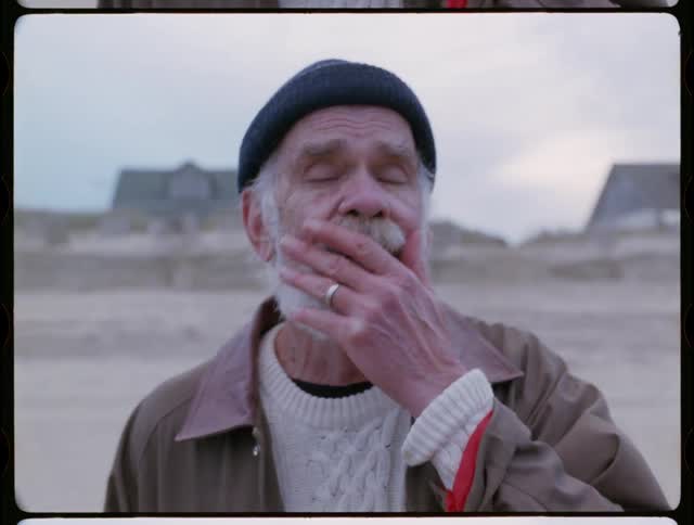 An elderly man cries on a beach