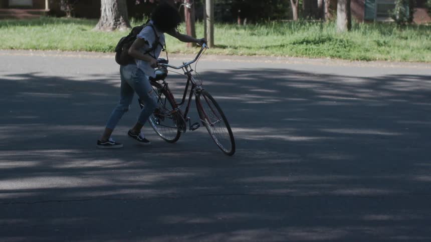 A woman dismounts a bicycle and pushes it