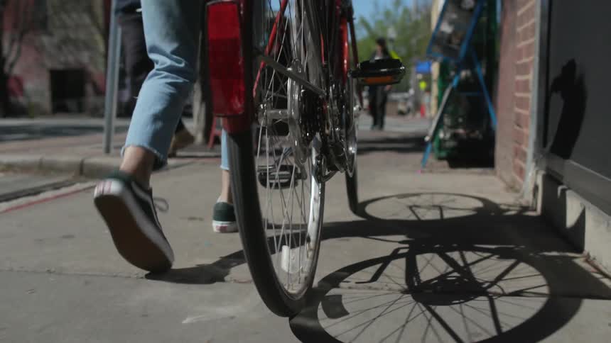 A woman pushes a bicycle on the sidewalk