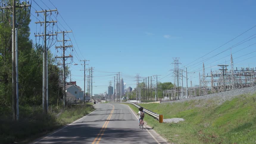 Woman rides her bike on a road in the outskirts of a city