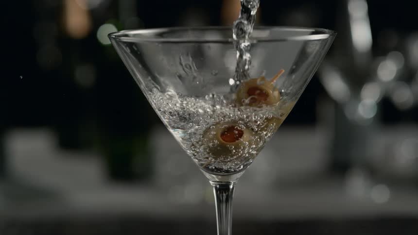 Alcohol is being poured into a cocktail glass over olives