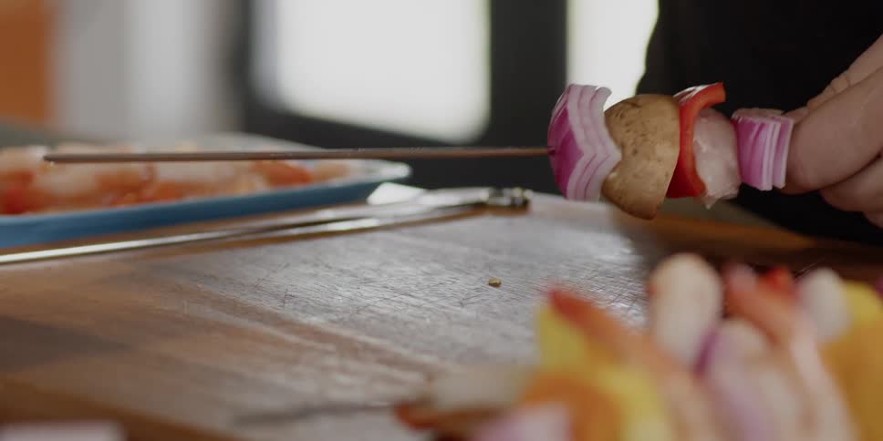 A man puts meat and vegetables on a skewer