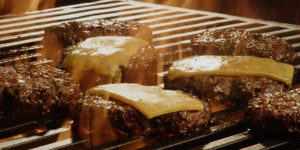The burgers on the grill are covered in flames
