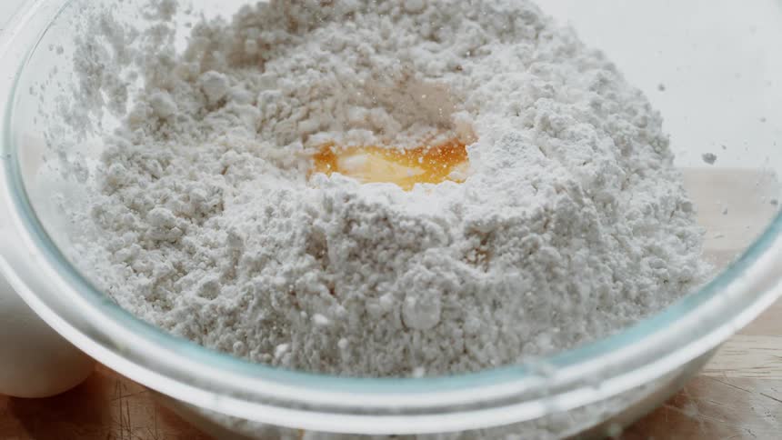 An egg is dropped into a bowl of flour