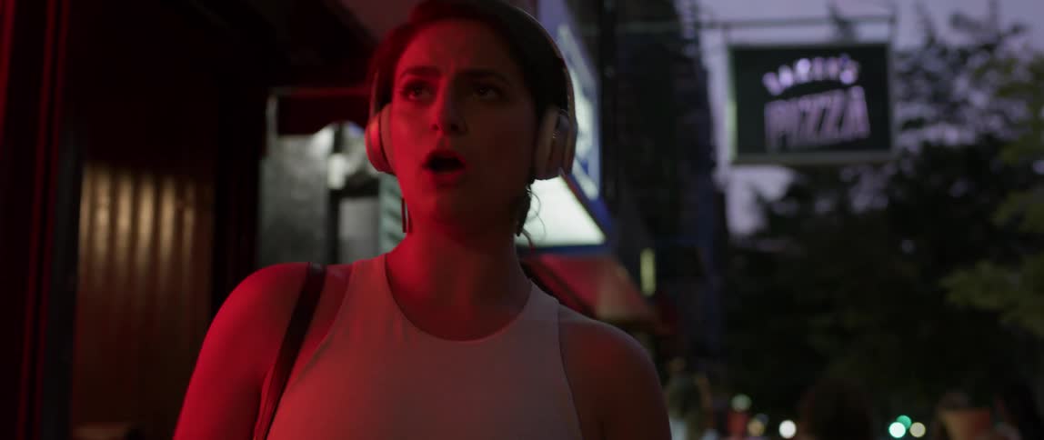 A woman dances and sings on a city sidewalk at night