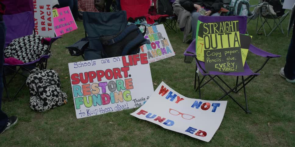 Protest signs lean against lawn chairs set up on the grass