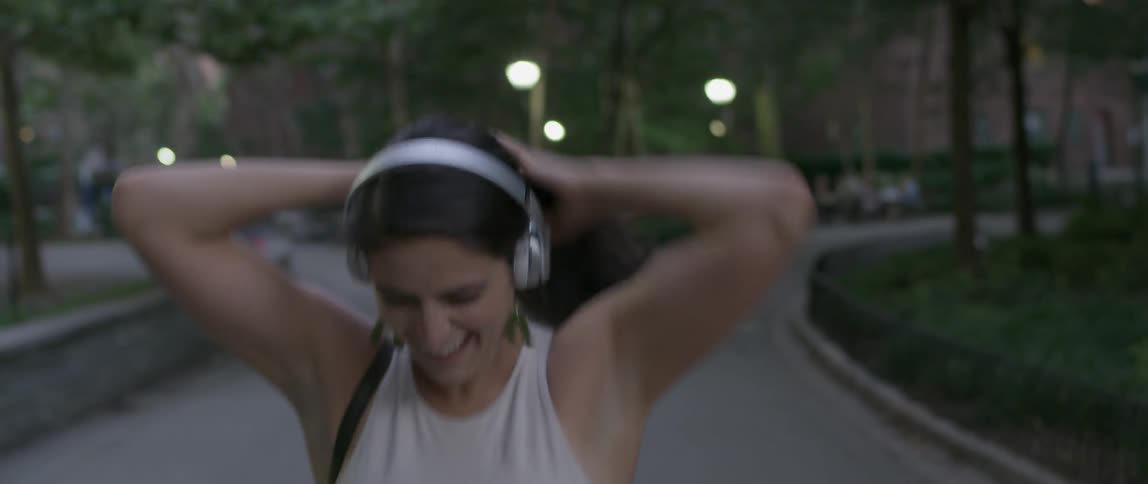 A woman sings and dances in a city park while wearing headphones