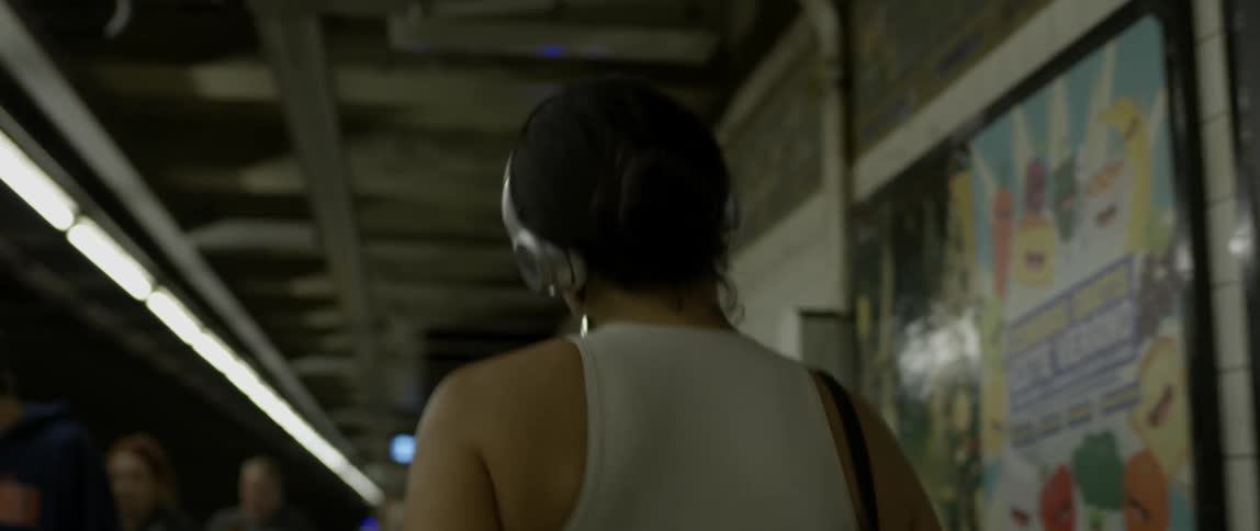 A woman wearing headphones dances while walking on a subway platform