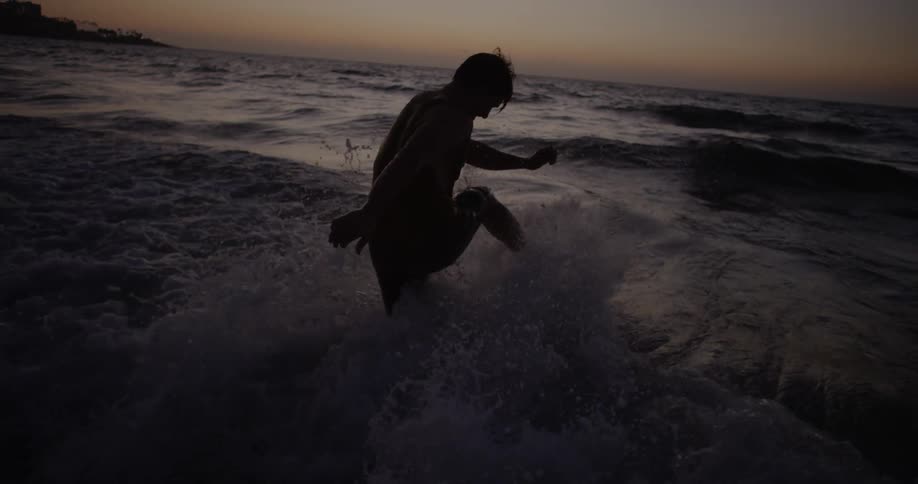 A man kicks ocean waves at dusk