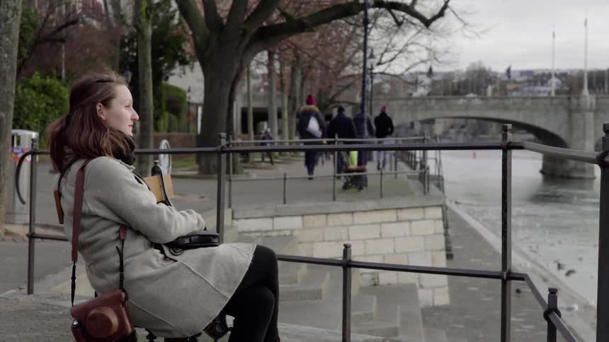 Woman sits behind a railing and looks at the river