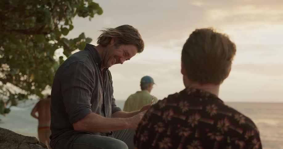 Two man laugh while talking on a beach at sunset
