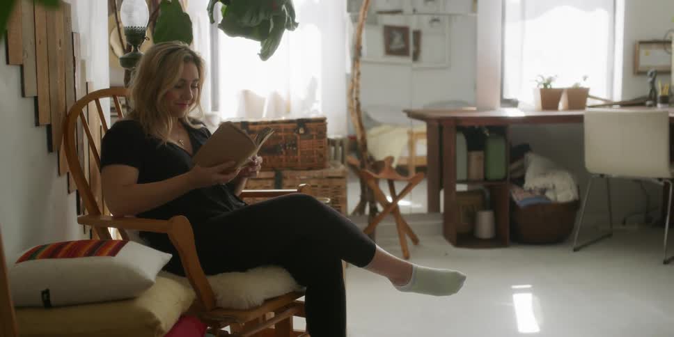 Woman sits on a wooden rocking chair reading a book