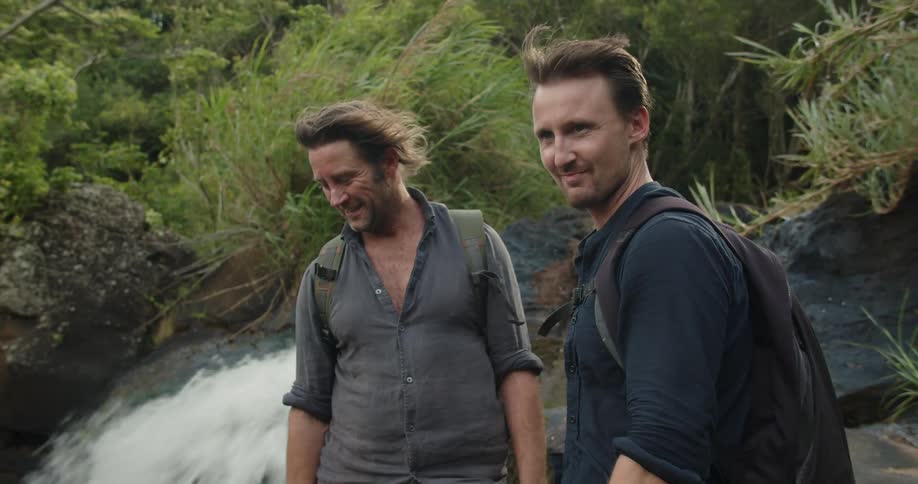 Two men watch the water flow over the rocks