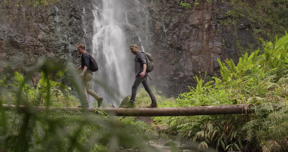 Two people walk on the log over the stream