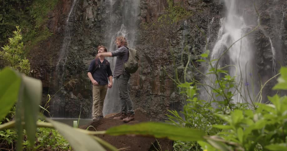 Hikers stand next to a waterfall in the wilderness