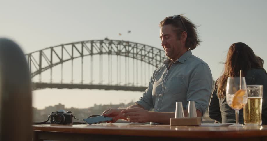 A man smiles and puts down his phone while sitting outside at sunset