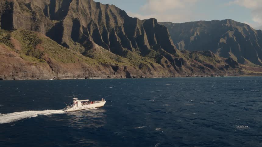 White boat travels in the water near a mountain