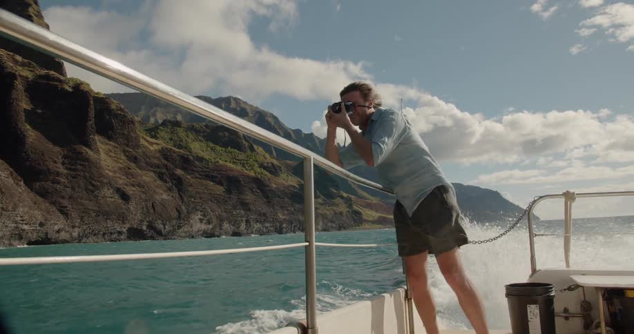 Man standing on a boat near the mountains taking pictures