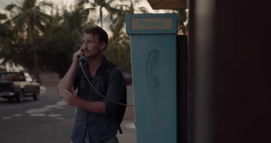 Man talks on a pay phone at sunset