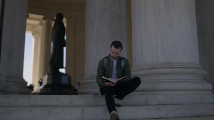 A man sits on the stone steps reading a book