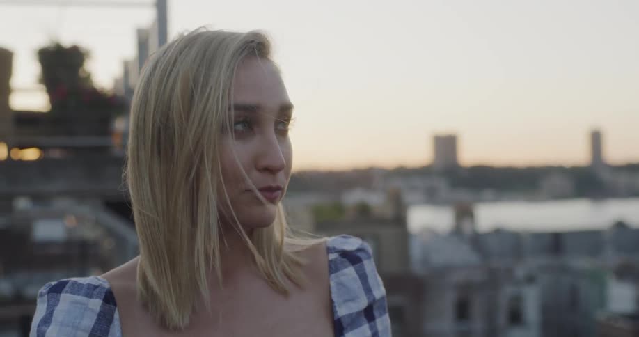 A woman is smiling and talking outside on a rooftop at sunset