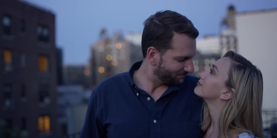 Man and woman kiss on a building rooftop at dusk