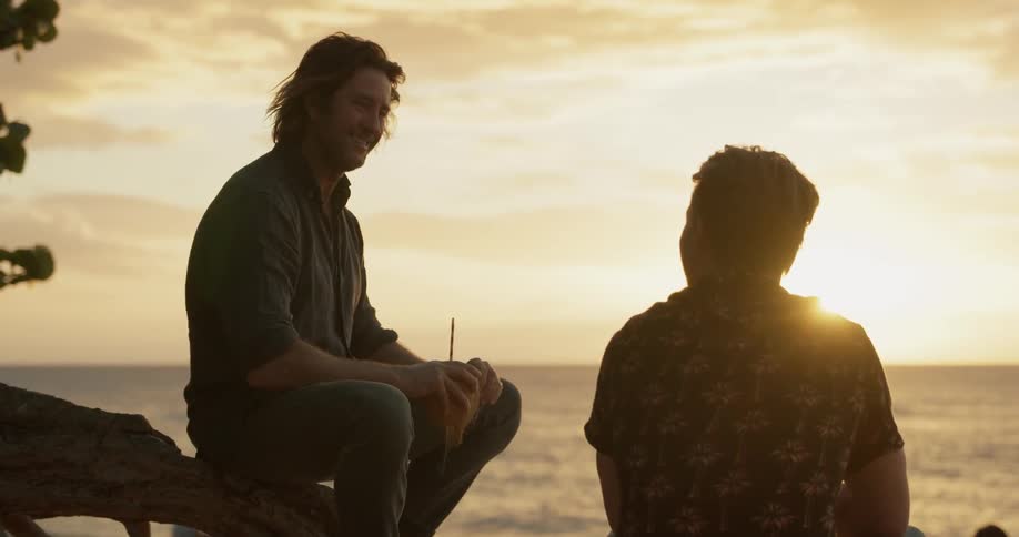 Two men sit on the beach talking at dawn