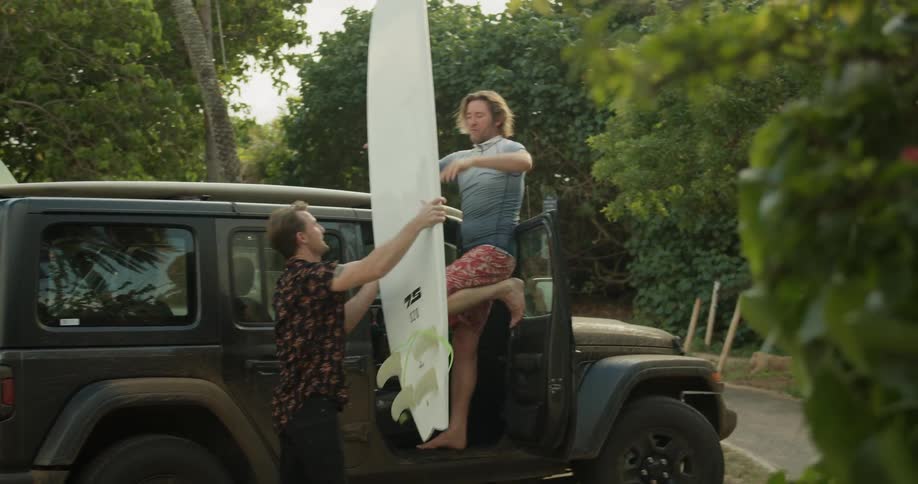 Two men getting a surfboard off a jeep