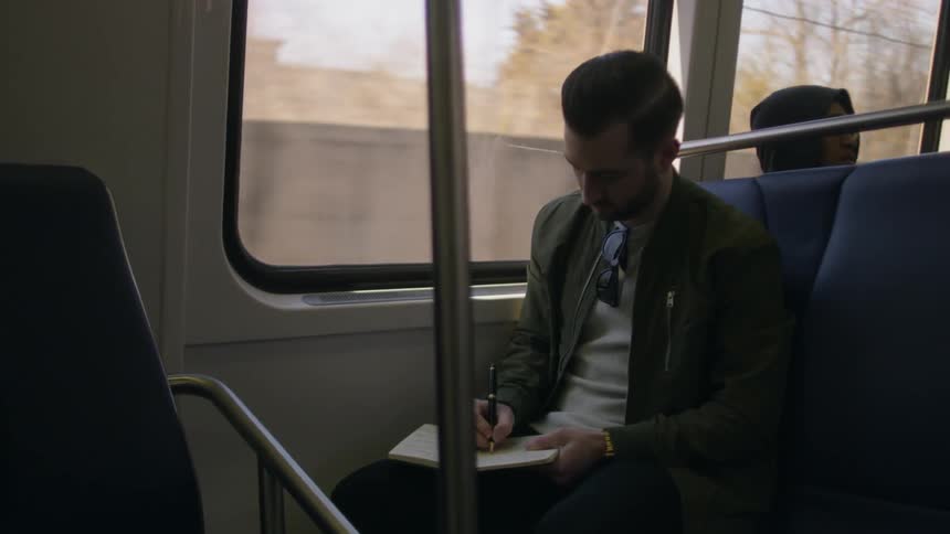 Man writes in a notebook as he travels in a train
