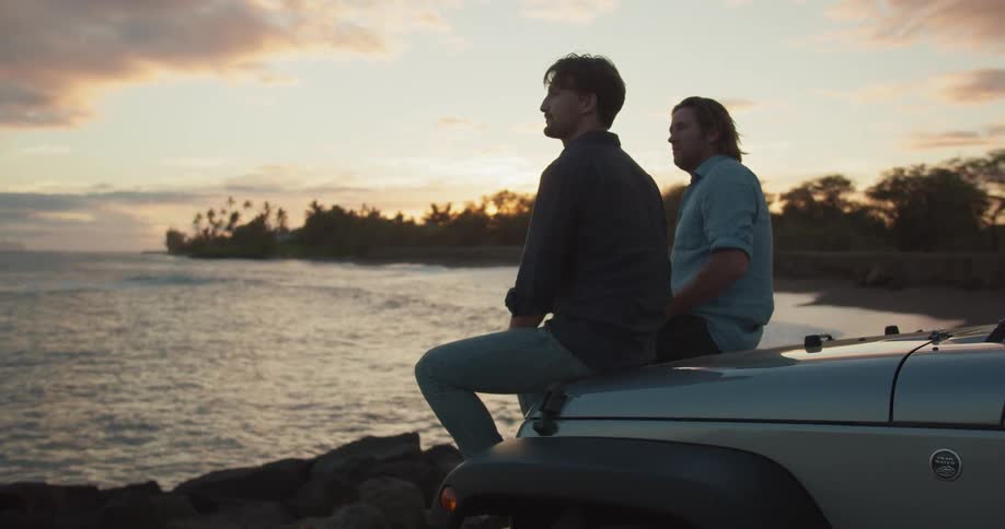 Two men are sitting on the hood of an suv and watching the sunset at a beach