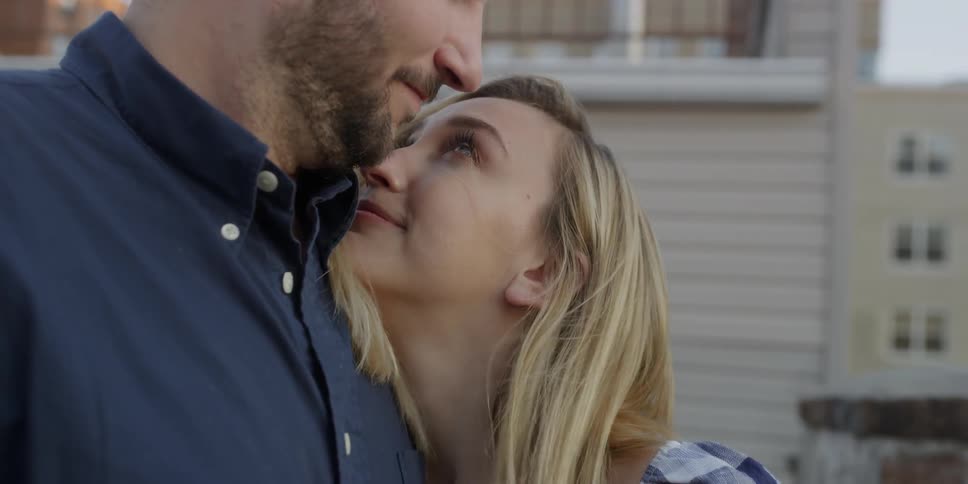 A man and woman embrace on a rooftop balcony