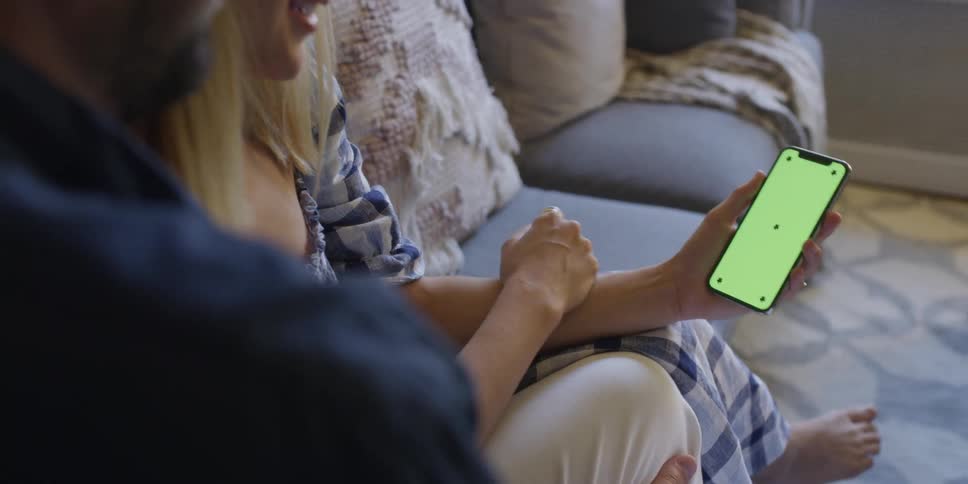 Man and woman sit on a sofa as the woman holds a cellphone