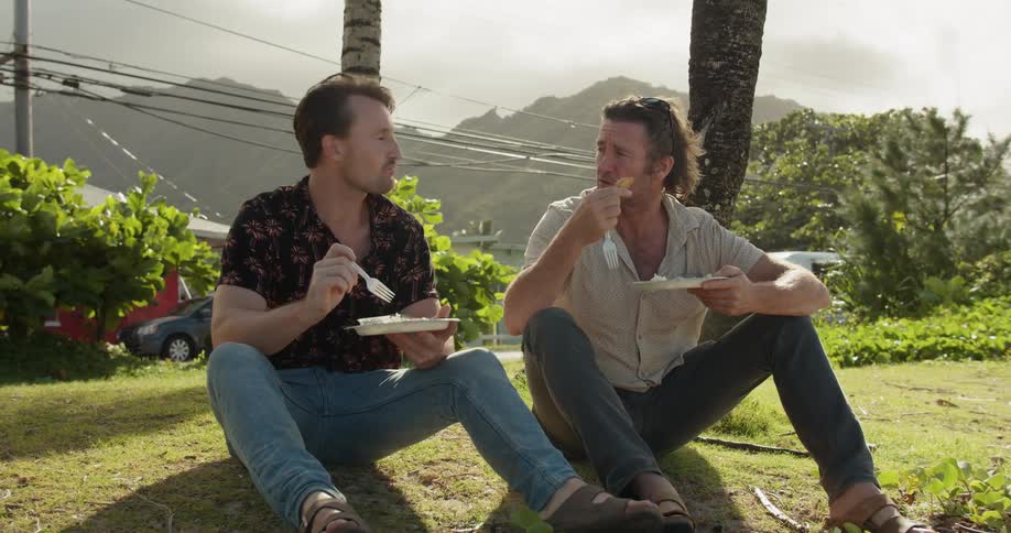 Two men talk while eating on the ground