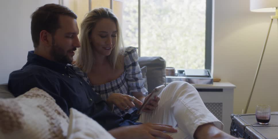 A man and woman use a phone together on the couch
