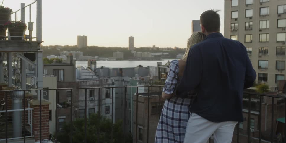 Man and woman stand together on a balcony looking out at the city