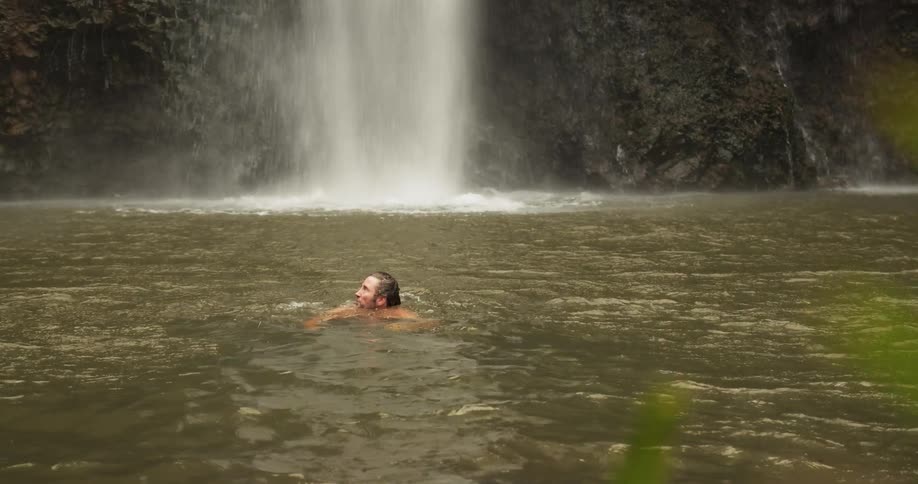 A man swims in the water by the waterfall