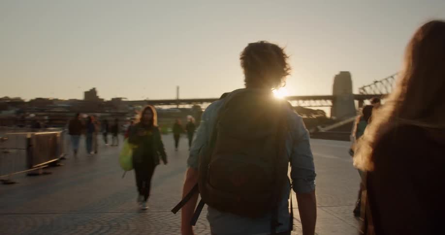 A man carries a backpack on the walkway by the bridge