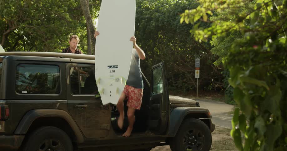Man pulls a surfboard off a car roof