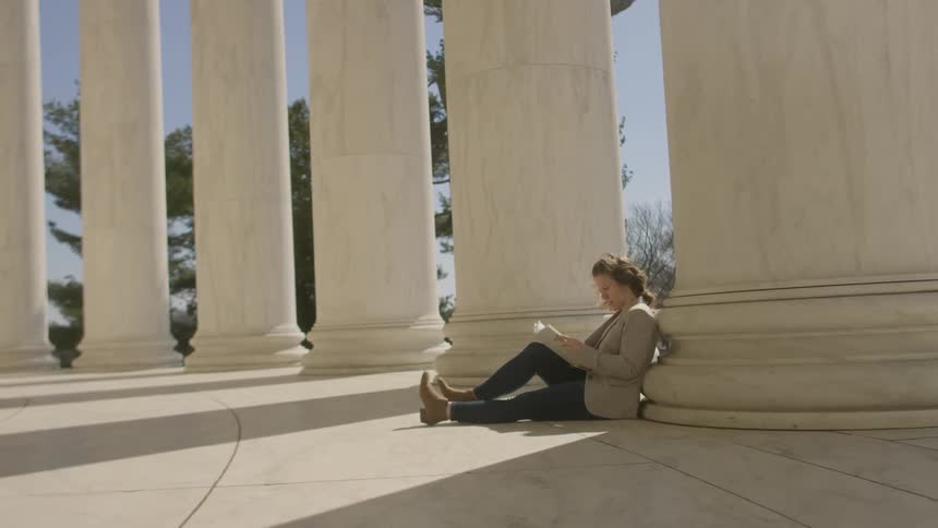 A woman sits against a concrete column