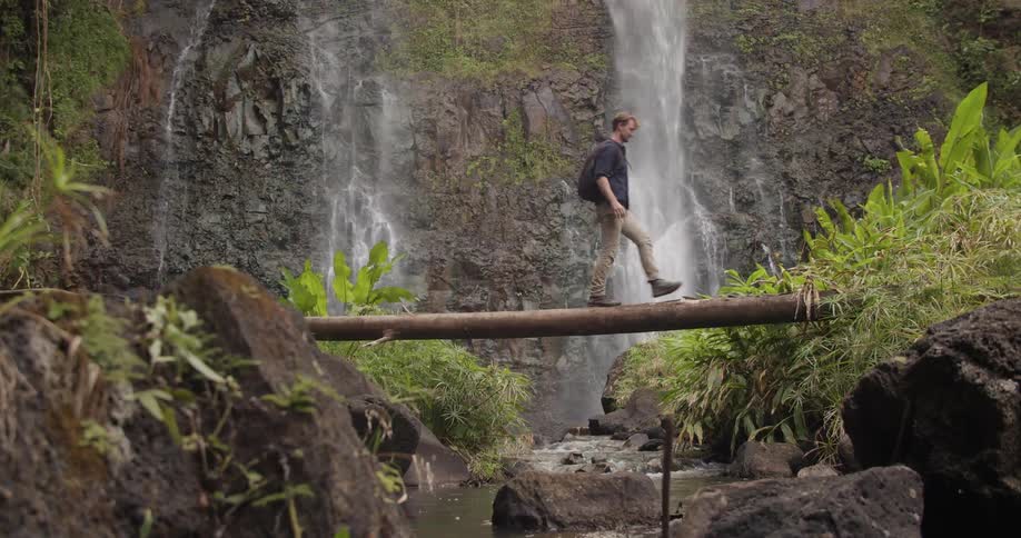 A man walks on a log over a stream