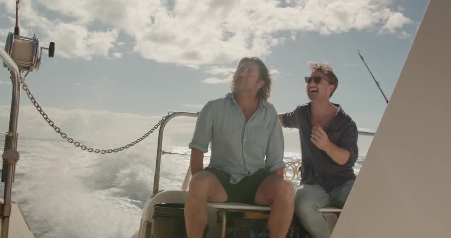 Two men ride on the back of a speeding boat