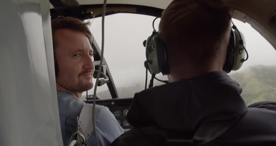 Two men fly over mountains in a helicopter