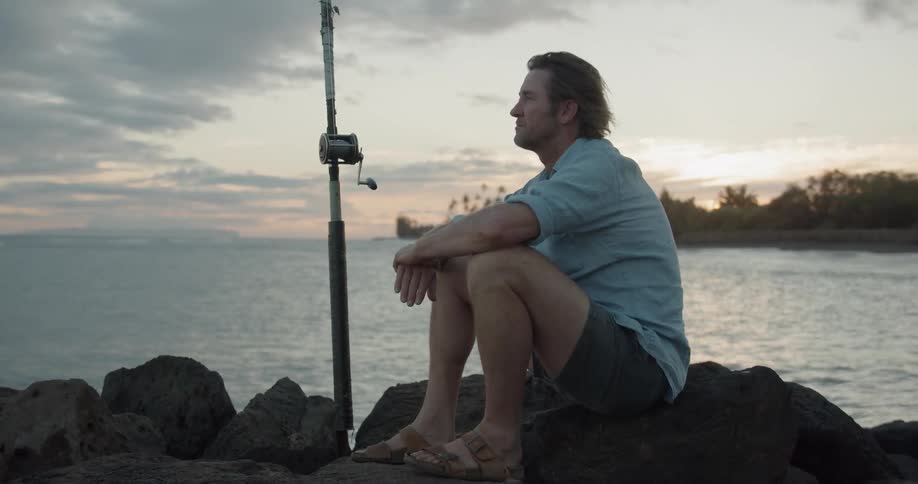 A man sits on the rocks with a fishing pole